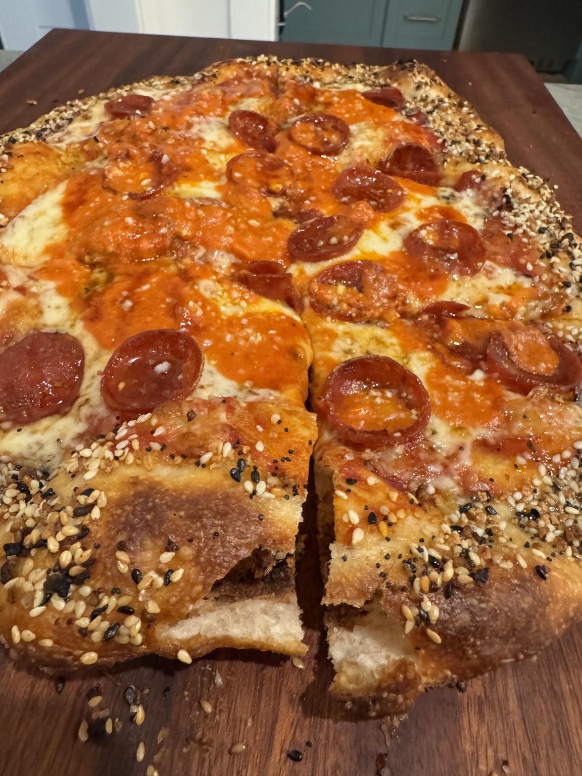 Greg’s pepperoni pizza with a seeded crust, sliced on a wooden board